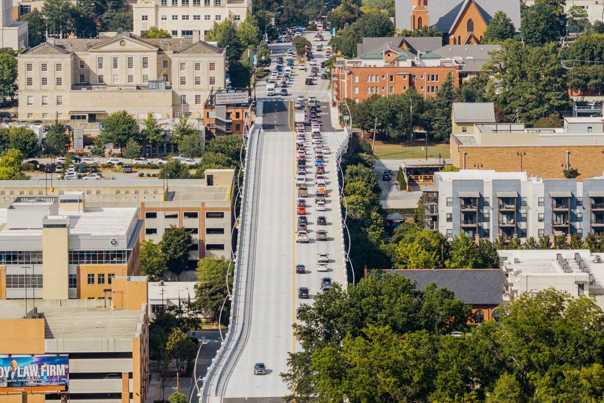 Traffic crossing a bridge into downtown Greenville, queued in one direction, with the county buildings on the rise beyond.